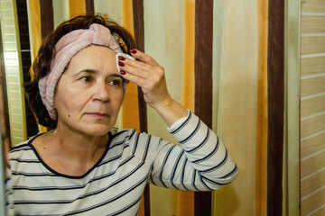Elderly woman cleansing her face with cotton pad in front of a mirror