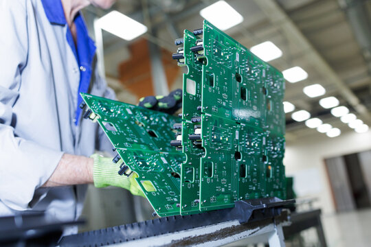 Worker handling assembled green circuit board panels at electronics factory