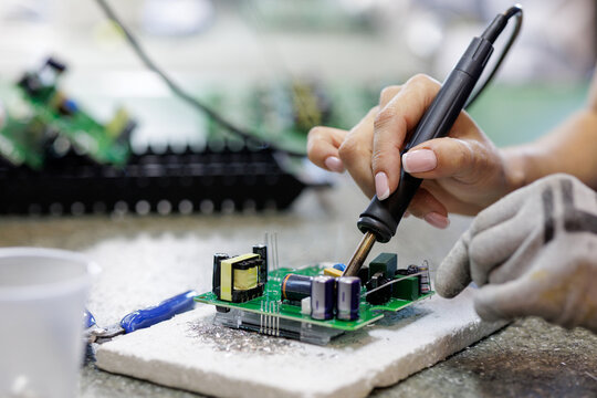 Female technician soldering electronic circuit board at industrial workshop - Powered by Adobe