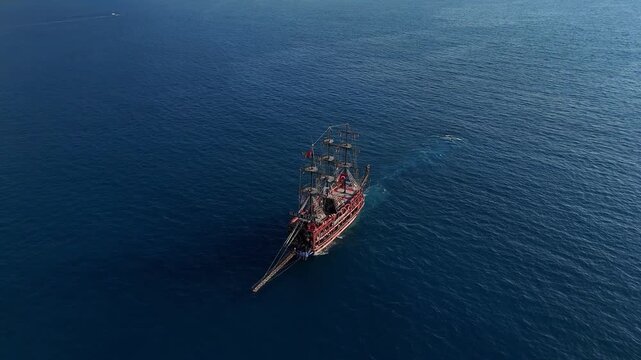 Aerial view of a large pirate-style tour ship sailing across the deep blue sea in Turkey on a sunny day. Calm water, clear sky, and smooth movement of the boat.