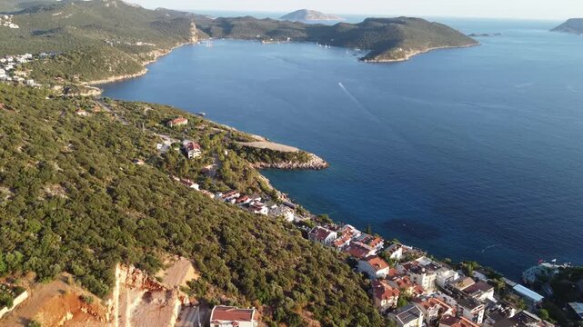 Aerial drone shot showing tranquil peninsula with island dotted horizon along coastal waters near Akyaka in Mugla, capturing green hills, seaside homes, calm blue sea, and warm late afternoon light