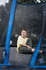 Obraz premium Smiling child sitting and relaxing on a trampoline after jumping
