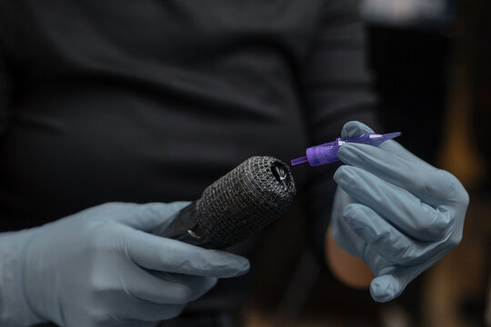 tattoo artist in gloves preparing a tattoo machine, attaching a sterile needle cartridge before a session in a professional studio.