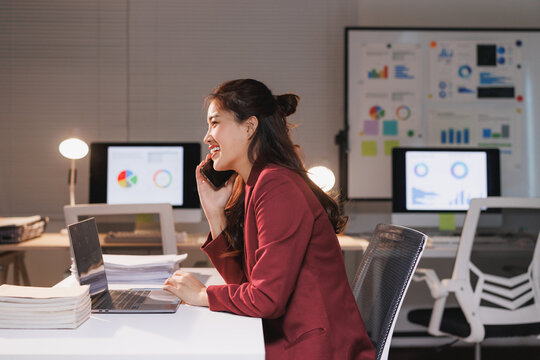 Smiling asian businesswoman discussing business on phone late night