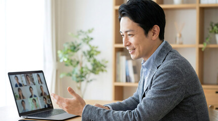 Smiling Asian man in a video conference working from home on a laptop connecting with colleagues online