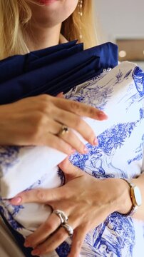 Close-up of a woman's manicured hands gently touching and feeling the soft texture of new, clean bed linen in solid dark blue and white Toile de Jouy pattern, emphasizing quality and comfort.