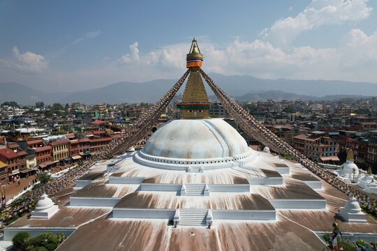 An aerial view of Boudhanath Stupa, Kathmandu, showcasing its majestic dome, colorful prayer flags, and the surrounding city&mdash;a serene Buddhist landmark from above.