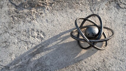 A metallic atom model with a central sphere and looping electron orbitals resting on a dusty surface. Concept Metallic atomic model, Central sphere nucleus, Looping electron orbits