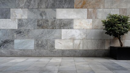 Gray rectangular stone wall and tiled floor with a small tree in a planter on the right. Concept Gray stone wall backdrop, Tiled floor texture, Small tree in planter, Minimalist urban setting