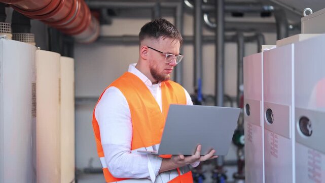 Professional engineer with glasses, wearing safety vest, intently monitors industrial systems using laptop. Displays focused attention and precision while ensuring efficient operations.
