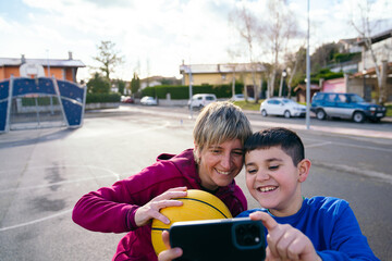 Happy mother and son bonding outdoors, capturing a joy filled moment with a smartphone and basketball on the court