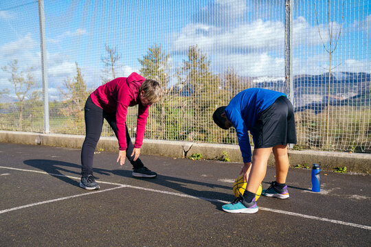 Mother and son doing warm up stretches together on an outdoor basketball court, preparing for exercise and activity