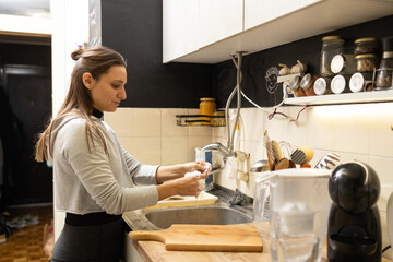 Woman washing dishes by kitchen sink