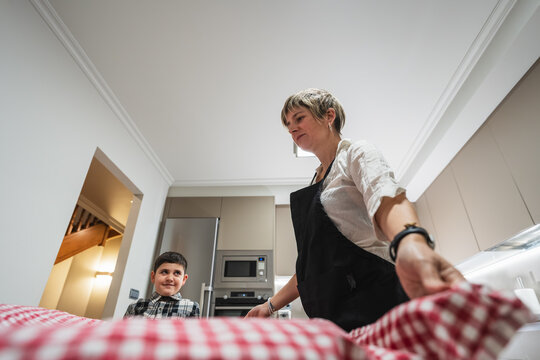 Mother and son preparing a meal together in a modern kitchen, spreading a checkered tablecloth on a table