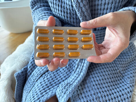 Adult woman holding blister pack of pills, vitamins at home, close-up health and wellness concept. Daily vitamin supplement routine