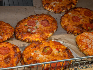 Ready mini baked pizzas with yellow cheese and salami, pizzeria in a bakery