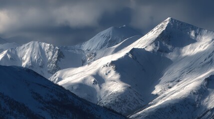 Dramatic snow covered mountain peaks with dark clouds and sunlight winter landscape