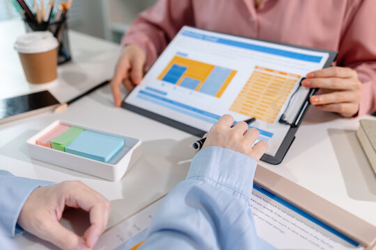Two female colleagues discussing business reports together in a modern office environment, representing teamwork, data analysis, and collaboration in a start-up company setting.