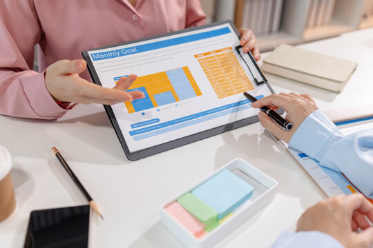 Two female colleagues discussing business reports together in a modern office environment, representing teamwork, data analysis, and collaboration in a start-up company setting.