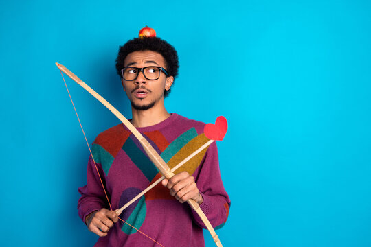 Young man with vintage bow and arrow on blue background showcasing trendy style and quirky charm in casual fashion.