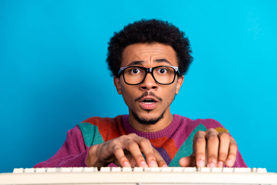 Young man typing on a keyboard while looking surprised against a bright blue background with a stylish sweater