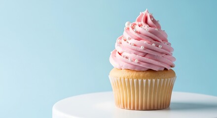 A single vanilla cupcake with tall swirl of pink frosting and white sprinkles sitting on a white pedestal against a light blue background
