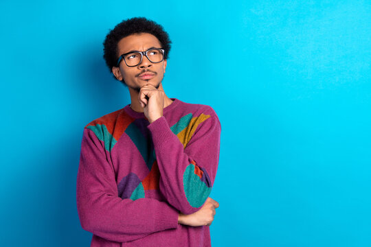 Funny man in colorful sweater thinking and looking curious while standing against a blue background