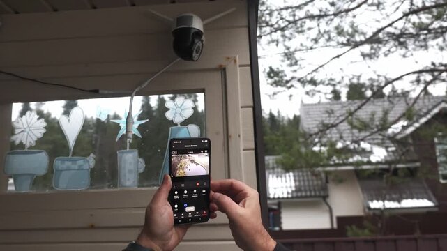 Hands holding hold smartphone that controls outdoor security camera. control home using smart home mobile app. High quality 4k footage