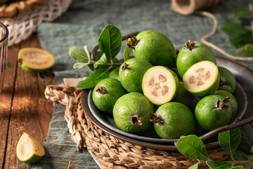 A rustic still life with ripe pineapple guavas, some cut open to reveal the fleshy pulp, on a small plate and in a basket