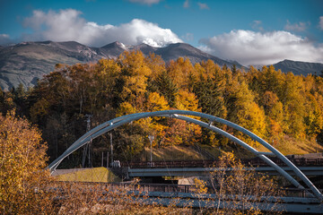A suspension bridge with vibrant golden autumn trees, a blue sunny sky, and a high mountain landscape in the background, at Shirahige waterfall, Hokkaido, Japan