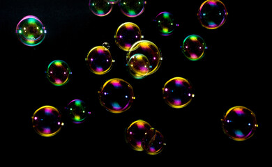 Colorful Soap Bubbles with Green, Orange, Red, and Gold Colors on Black Background - Abstract Bubble Photography Showing Multiple Floating Spheres with Vibrant Iridescent Light Reflections

