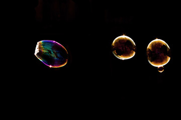 Soap Bubbles Composition with Large Iridescent Bubble and Golden Bubble Pair on Black Background - Abstract Bubble Photography Showing Mixed Sizes with Colorful Reflections and Light Effects

