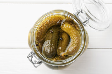 Pickled cucumbers in jar on white wooden table, top view