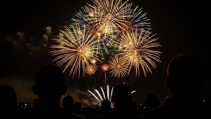 Spectacular fireworks display illuminates the night sky with vibrant colors and a crowd of silhouettes observing the celebration