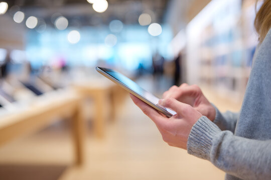 A customer using a tablet in a modern electronics store. Close-up of hands touching the screen while shopping for a new device during a sale