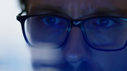 Man wearing glasses intensely focused on a glowing screen with data reflections