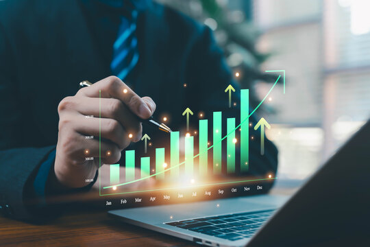 A businessman pointing at a glowing rising bar chart on a laptop represents financial growth, business analytics, performance improvement, digital data analysis, and strategic development for modern - Powered by Adobe