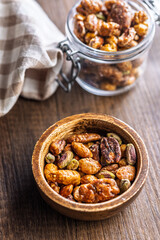 Nuts coated in sugar glaze in bowl on wooden table.