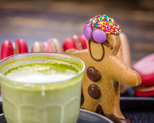 A gingerbread man with chocolate buttons is surrounded by red and cream-colored macarons.