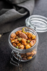 Nuts coated in sugar glaze in jar on black table.