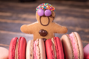 A gingerbread man with chocolate buttons is surrounded by red and cream-colored macarons.