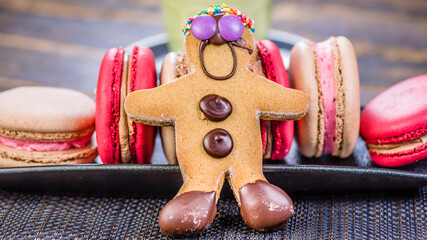 A gingerbread man with chocolate buttons is surrounded by red and cream-colored macarons.