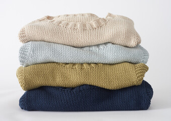 Stack of knitted sweaters folded in pastel colors on a white background