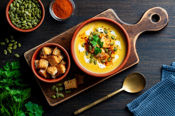 Delicious pumpkin cream soup with baked bread and pumpkin seeds in a ceramic bowl on a wooden table, closeup, top view. Healthy food concert