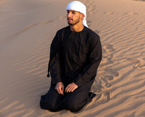 Arab man sitting on sand in the desert during golden hour, wearing traditional arab clothing. High quality photo