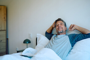 Mature man happily stretching and smiling in bed after a good night's sleep, feeling refreshed and ready for the day