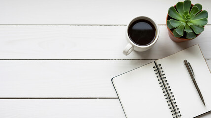 Overhead view of a coffee cup notebook pen and succulent on a white wooden desk