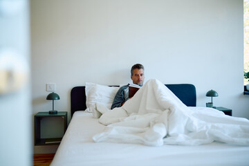 Man is unwinding in bed, clad in pajamas, engrossed in a book, and savoring a peaceful morning in a...