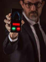 Business Man Holding a Smartphone Displaying a Critical Digital 'Warning' from an Unknown Hooded Cyber Threat