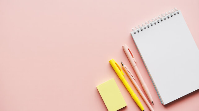 Flat lay of a blank notebook with pens and sticky notes on a pink background
